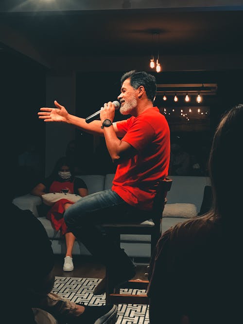 A Man in Red Crew Neck T-shirt and Blue Denim Jeans Sitting on Brown Chair