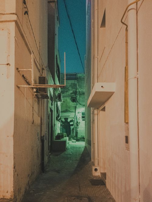 Free A narrow urban alley lit by ambient green lighting during nighttime. Stock Photo