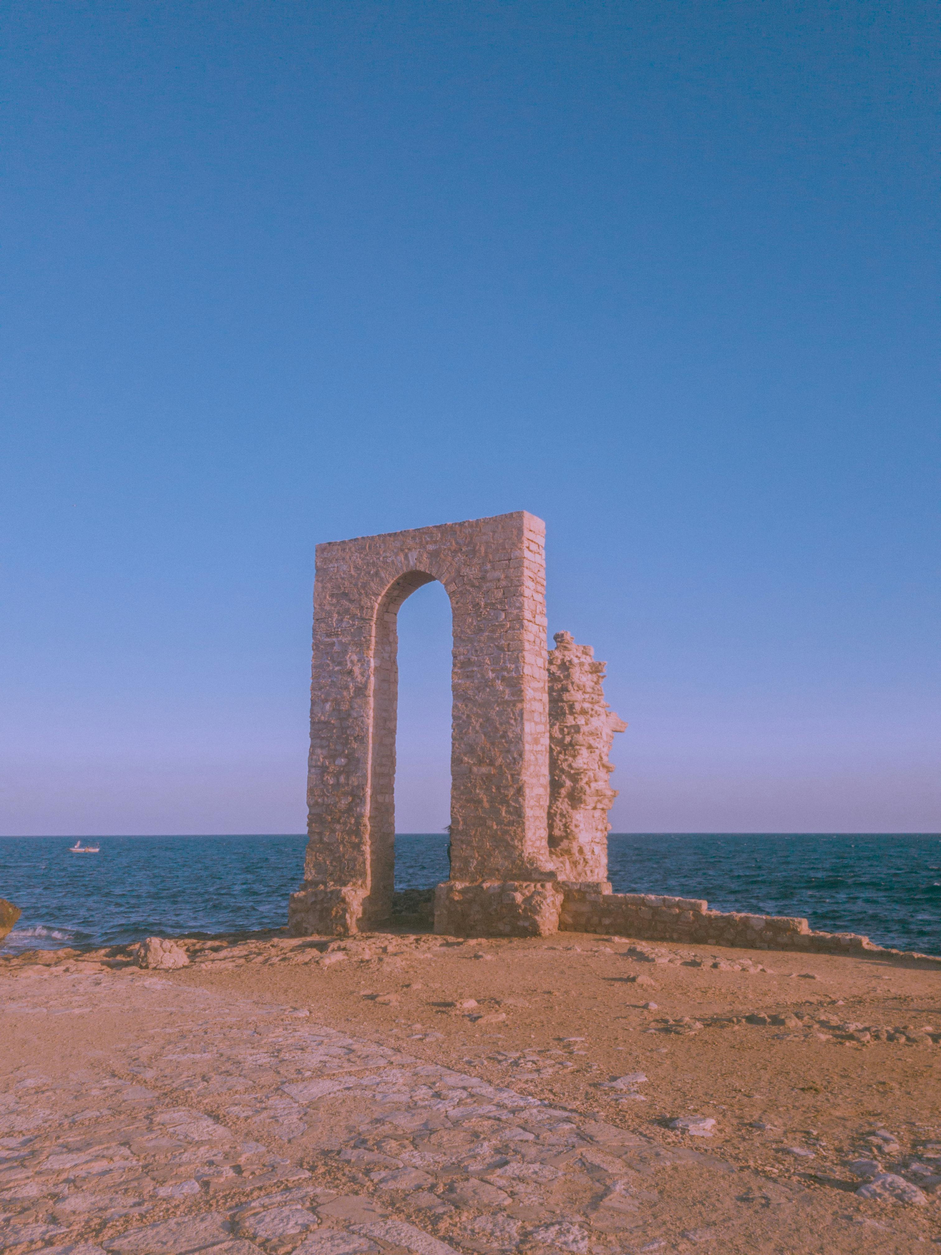 Serene ancient stone arch overlooking the ocean on a bright, clear day.