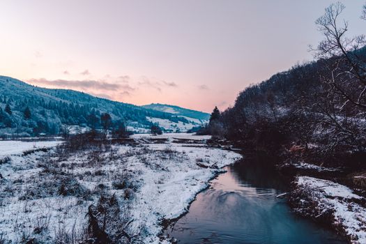 Captivating winter scene in Valea Seacă with mountains, a river, and pastel sunset hues.