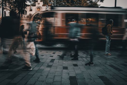 Blurred unrecognizable pedestrians walking on paved street near aged tramway in motion in old city