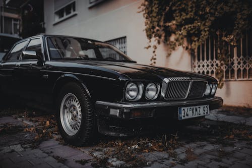 Shiny black vintage car with chrome polished details parked on paved street near old building in city