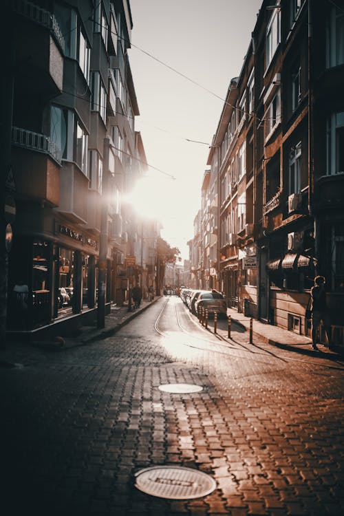 Cars parked on narrow paved road amidst aged residential buildings against sunrise sky in city