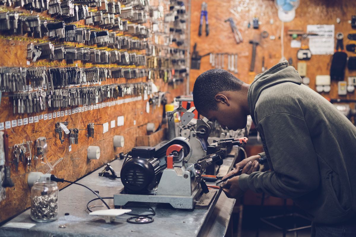 A young locksmith cutting a key on a key machine in front of a wall of key blanks