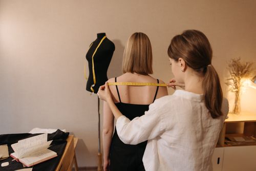 Free A tailor measuring a woman for a custom fit garment in a sewing workspace. Stock Photo