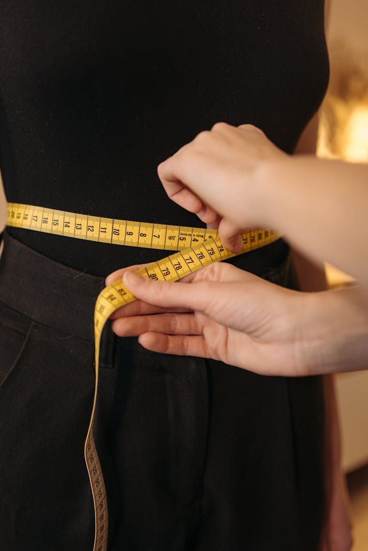 A Person Measuring A Woman's Waist