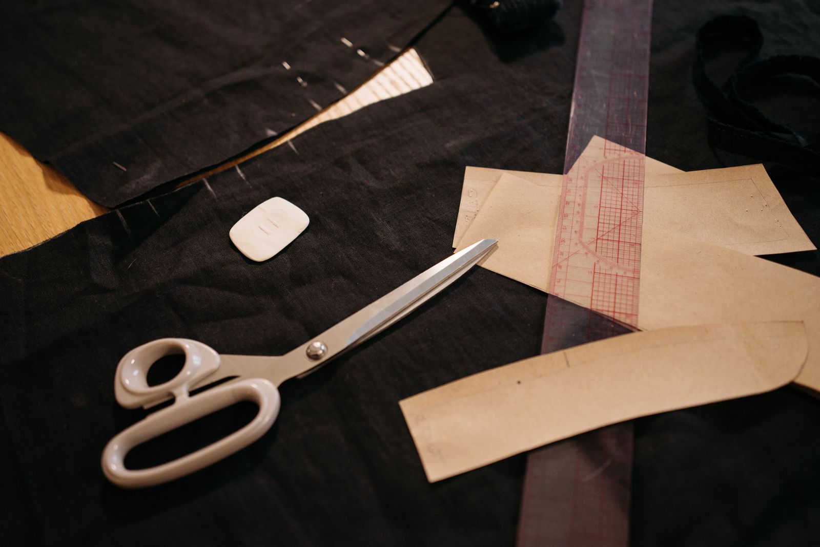 Shears, a pattern ruler and paper pattern pieces on dark cloth — Pavel Danilyuk on Pexels