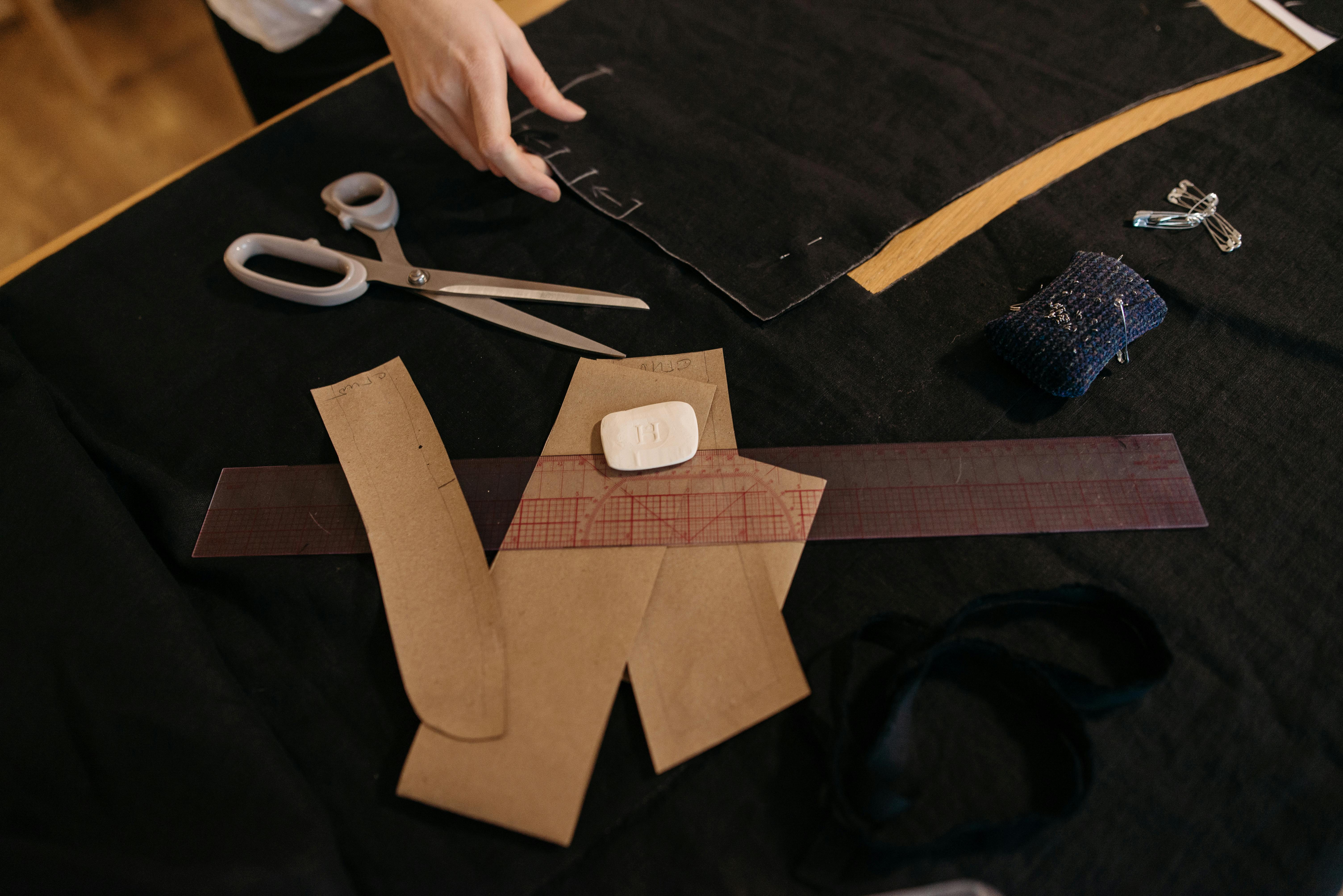A detailed view of a sewing workspace featuring scissors, patterns, and a measuring ruler.