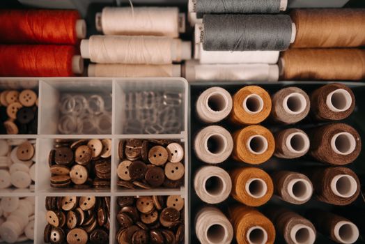 Overhead shot of organized sewing threads and buttons in a storage box, perfect for crafts.