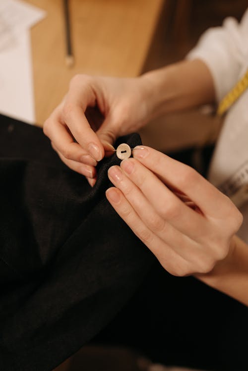 Person Sewing a Button on Black Cloth