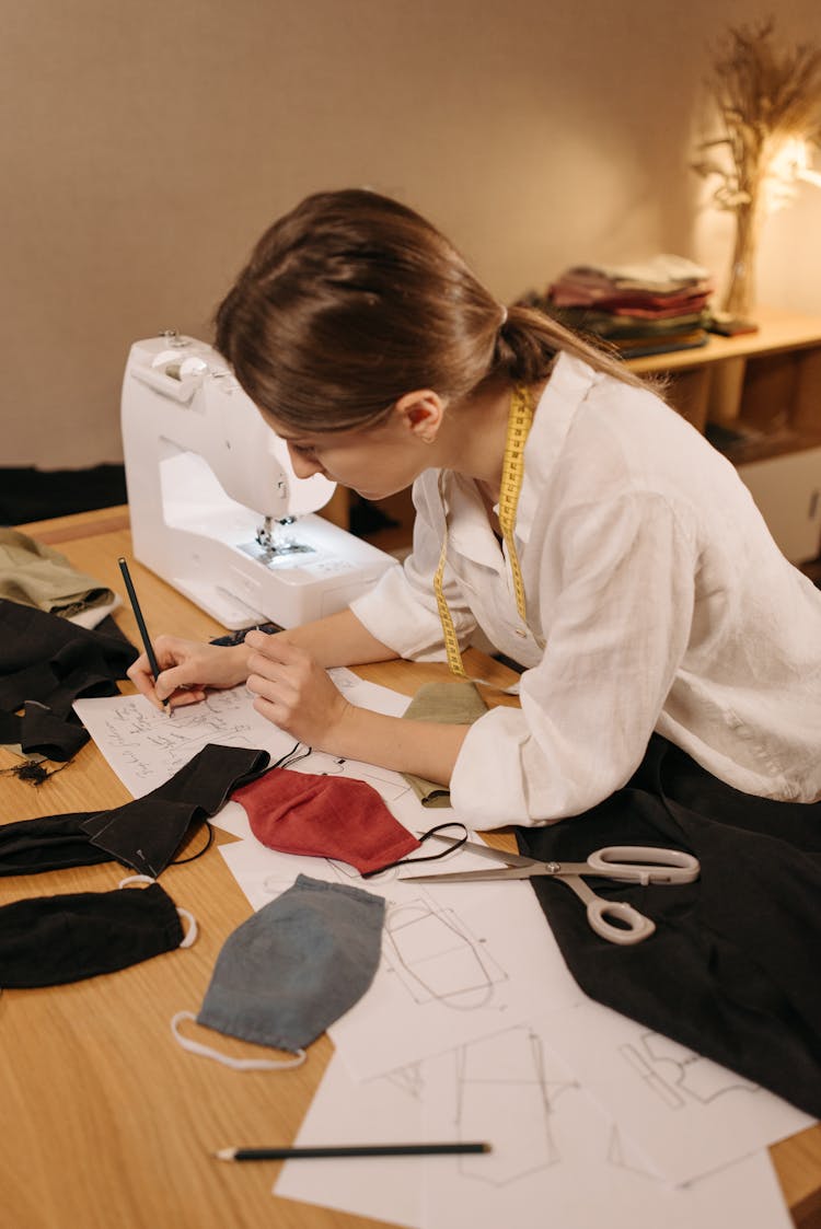 Dressmaker In White Long Sleeve Polo Shirt Sketching A Pattern On Paper