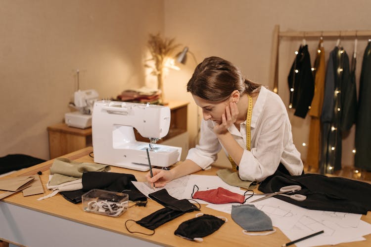 A Woman Drawing On A Paper While Making Face Mask Designs