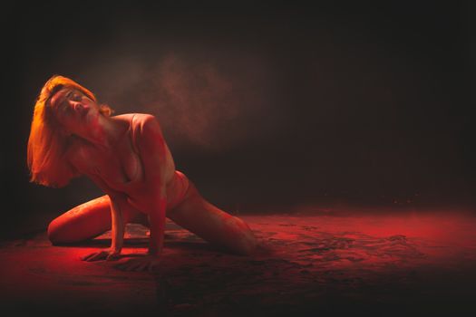Artistic expression of a woman dancer posing with colored red smoke in a dark room.