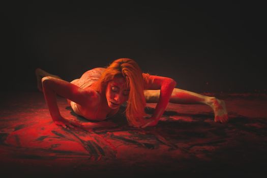 Contemporary dancer in a bodysuit creatively performing with red paint on the floor.