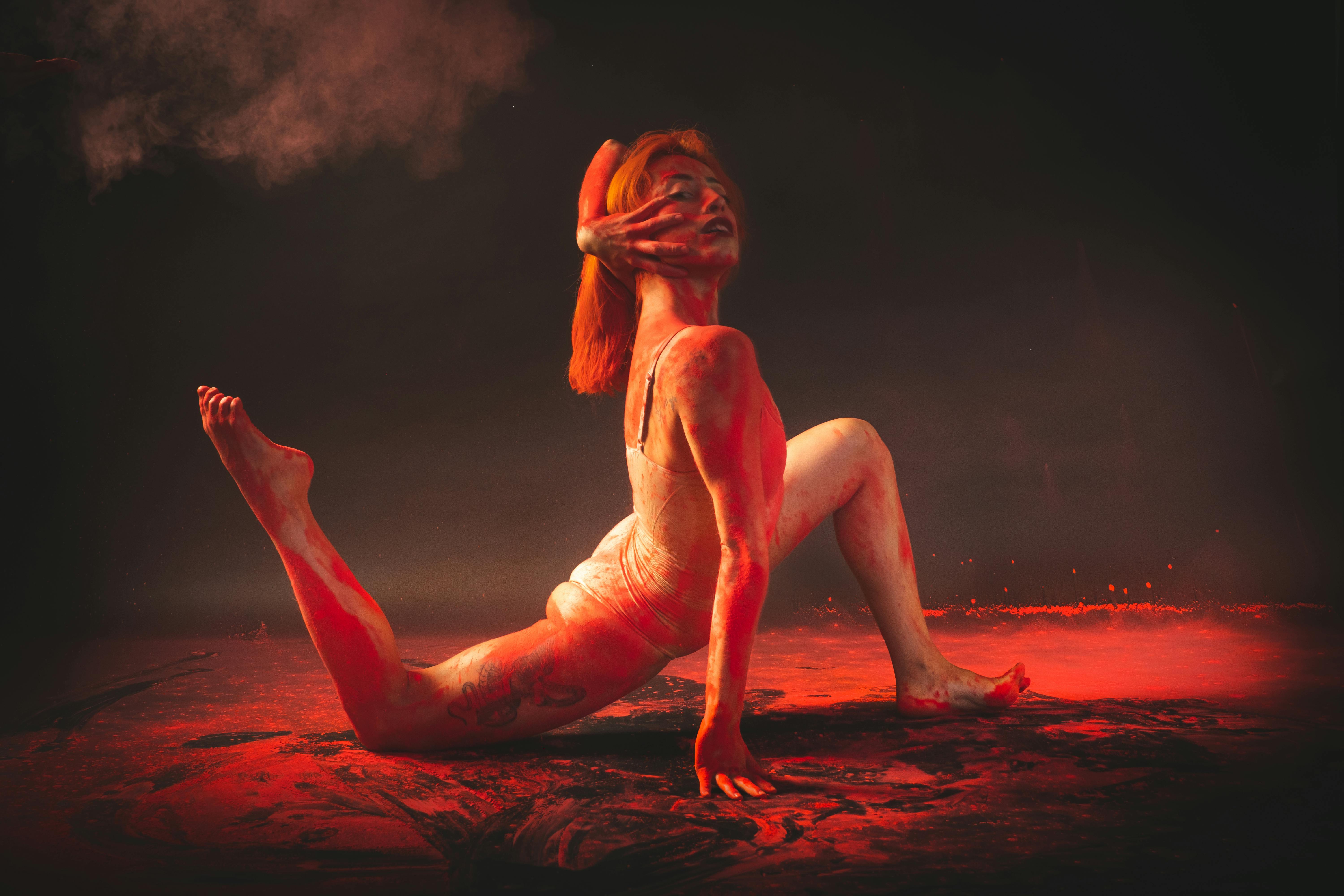 Free A female dancer performs an expressive pose with red lighting in a studio. Stock Photo