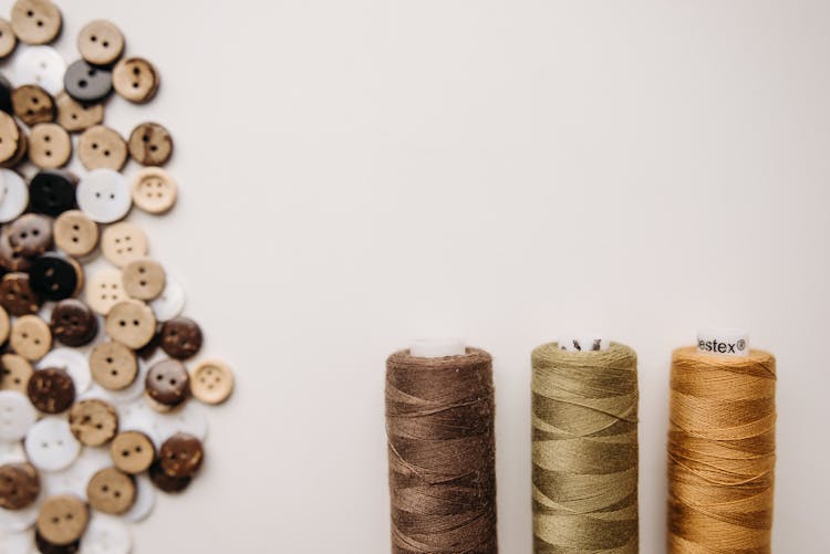 Spool Sewing Thread And Buttons On White Surface