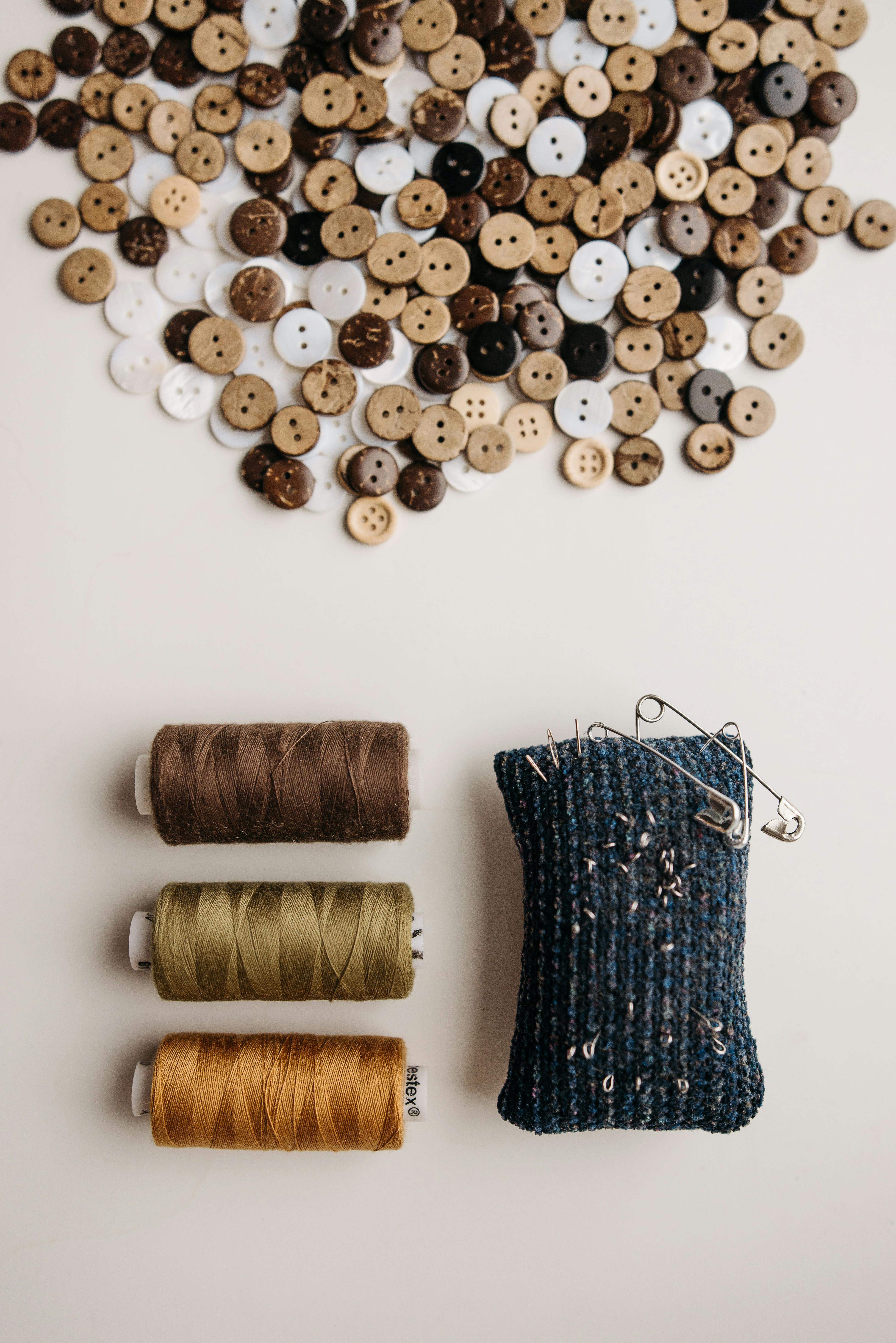 Stylish flat lay showcasing sewing threads, assorted buttons, and a pin cushion, perfect for crafting projects.