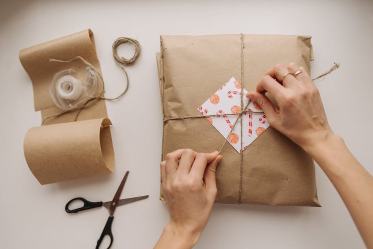 A Person Wrapping A Package Using Brown Paper