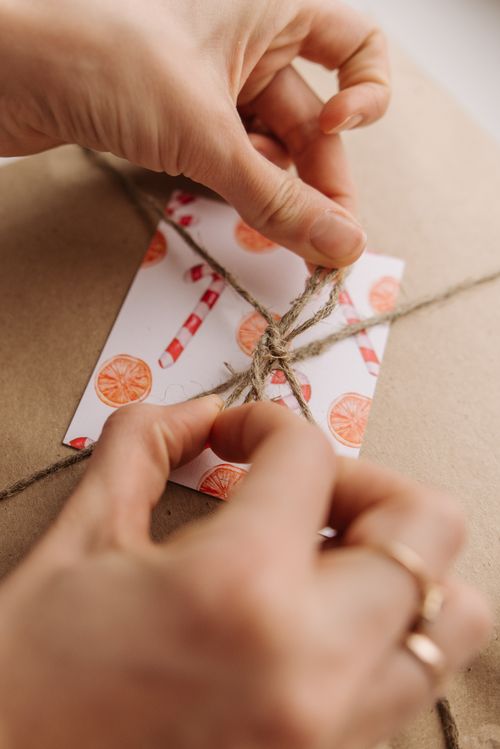 Free Close-up of hands tying twine on a gift with festive card, symbolizing care and creativity. Stock Photo