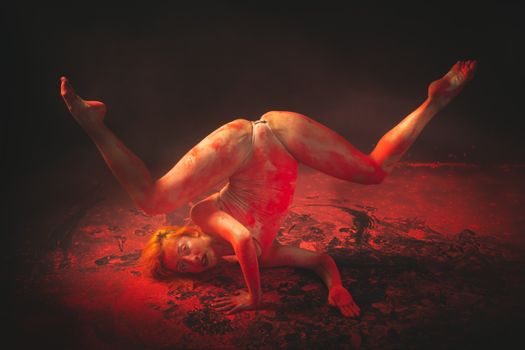 A flexible dancer performs an artistic pose surrounded by red powder, creating a dramatic visual effect.