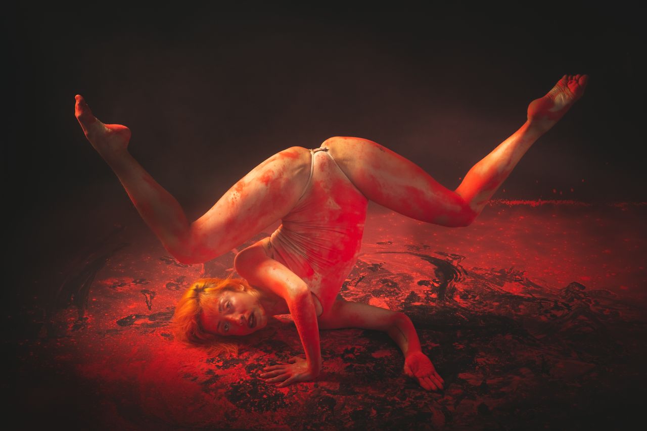 a flexible dancer performs an artistic pose surrounded by red powder c