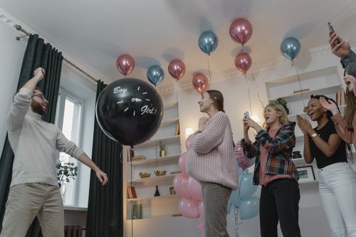 Free Group of friends celebrating a gender reveal party with balloons and excitement indoors. Stock Photo