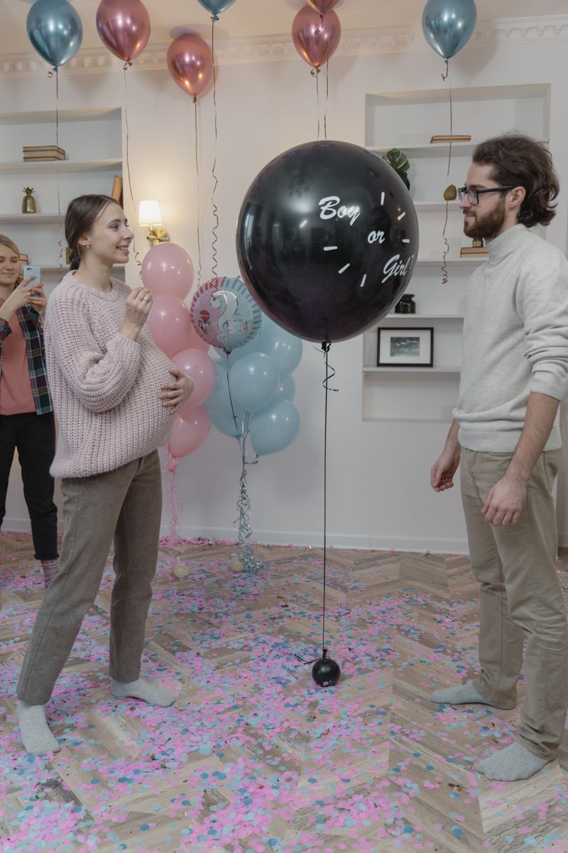 A couple enjoys a joyful moment during an indoor gender reveal party with friends.