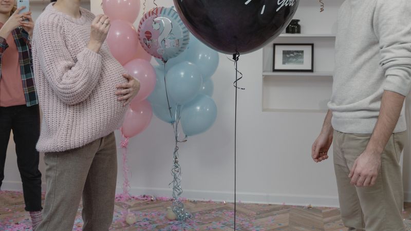 A couple enjoys a joyful moment during an indoor gender reveal party with friends.