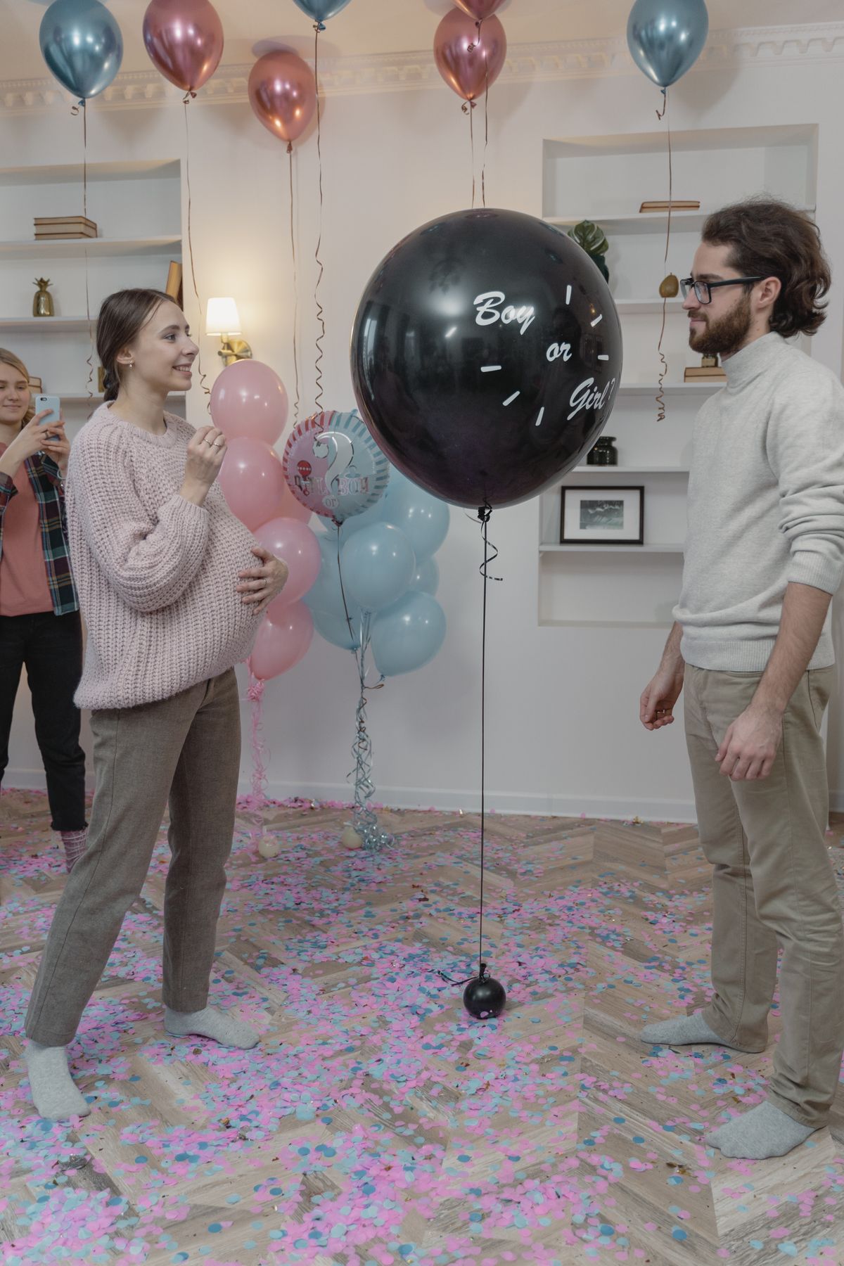 Werdende Eltern stehen bei einer Gender Reveal Party vor einem schwarzen Ballon