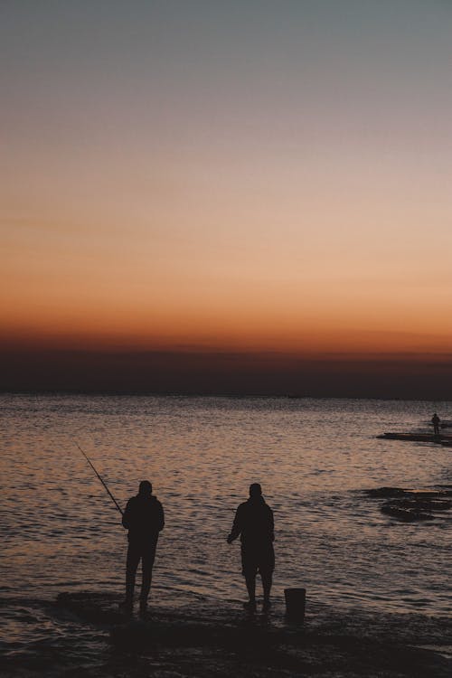 Vertical Shot of Fishermen Silhouettes and Sea with Horizon at Dawn