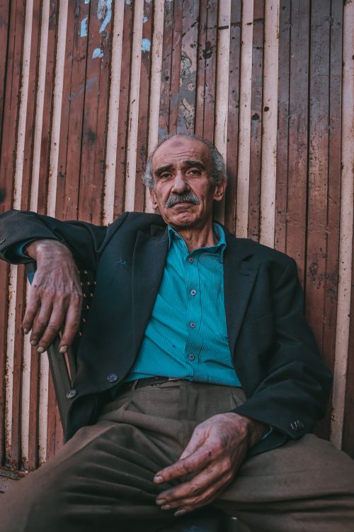Free A contemplative senior man with a mustache sitting indoors against a rustic wooden wall. Stock Photo