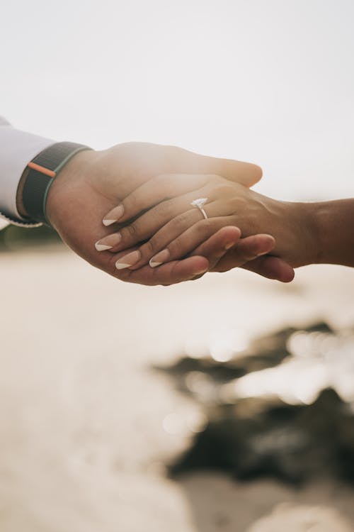 Faceless couple holding hands with ring on sandy coast
