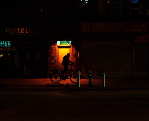 Free Silhouette of cyclist with bicycle walking on dark sidewalk Stock Photo
