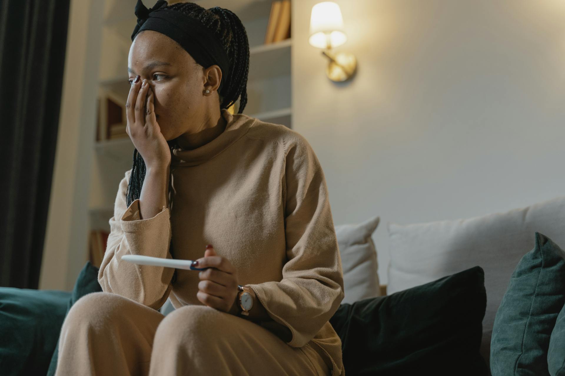 A woman indoors reacts emotionally while holding a pregnancy test.