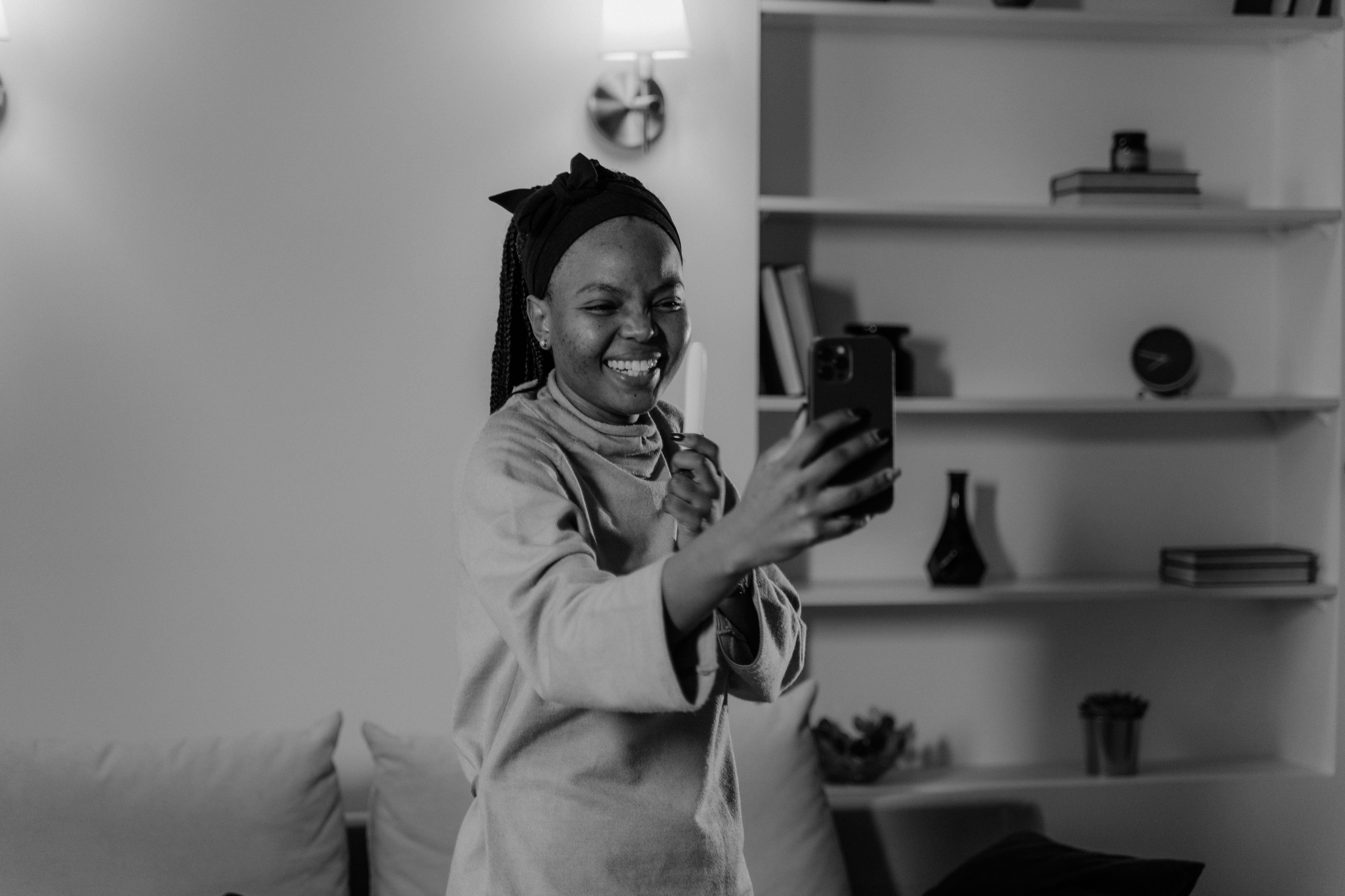 A happy woman takes a selfie indoors, capturing a joyful moment in grayscale.