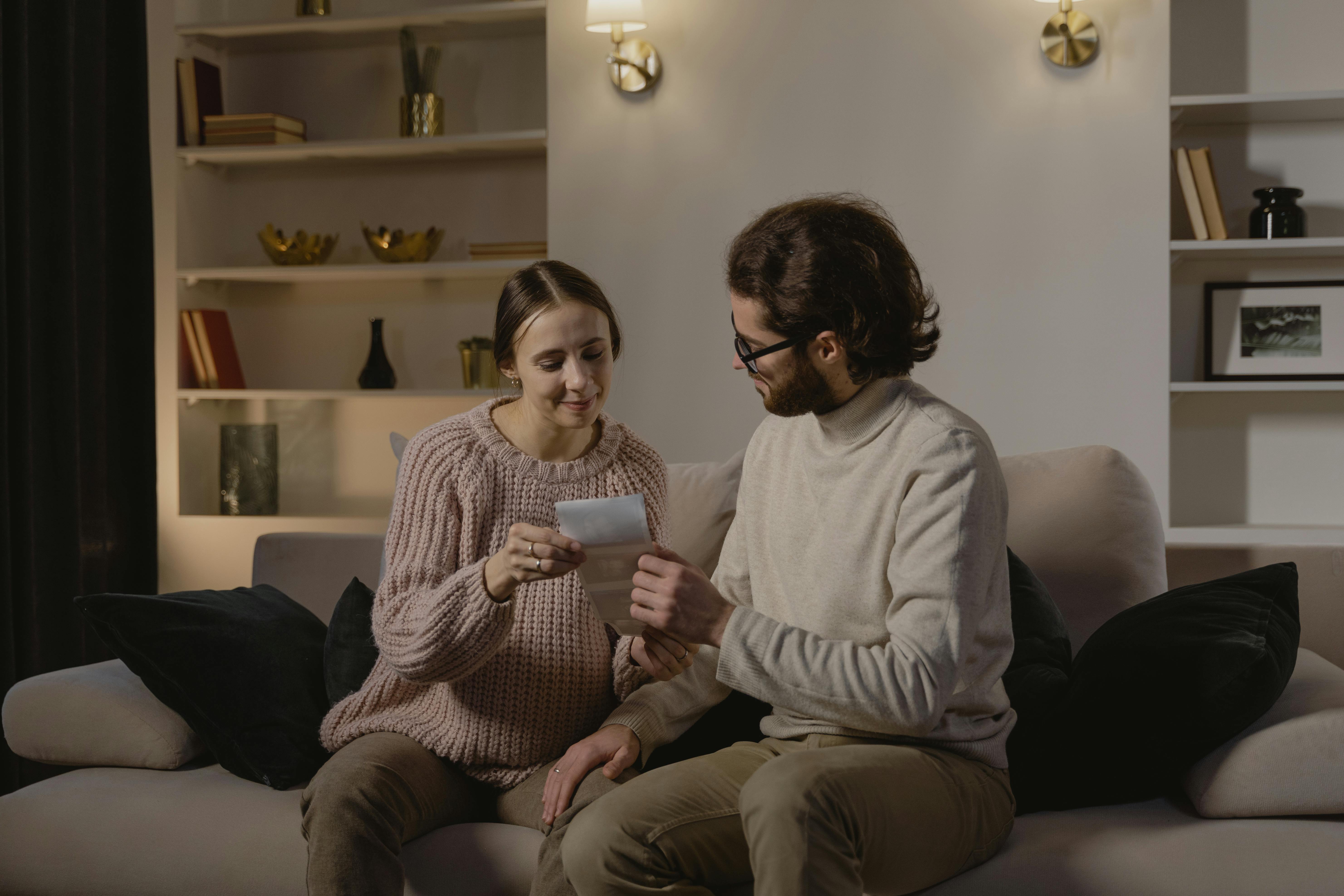 Free Expectant couple embracing joyous moment with ultrasound image on a cozy couch. Stock Photo