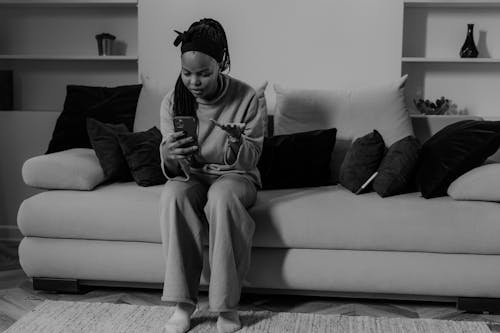 Free A Woman Sitting on the Couch while Holding Smartphone Stock Photo