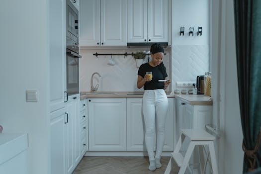 A woman standing in a modern white kitchen, holding a pregnancy test and glass of orange juice.