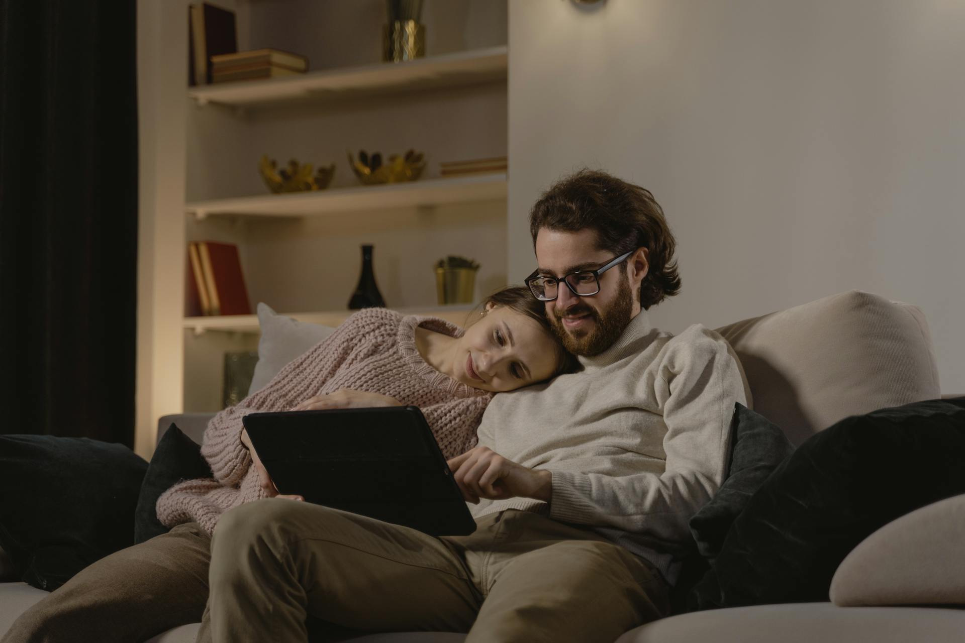 A Couple Sitting on Sofa while Looking at the Tablet Computer