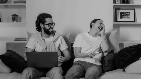 A happy couple sitting on a sofa, laughing and enjoying time together indoors.