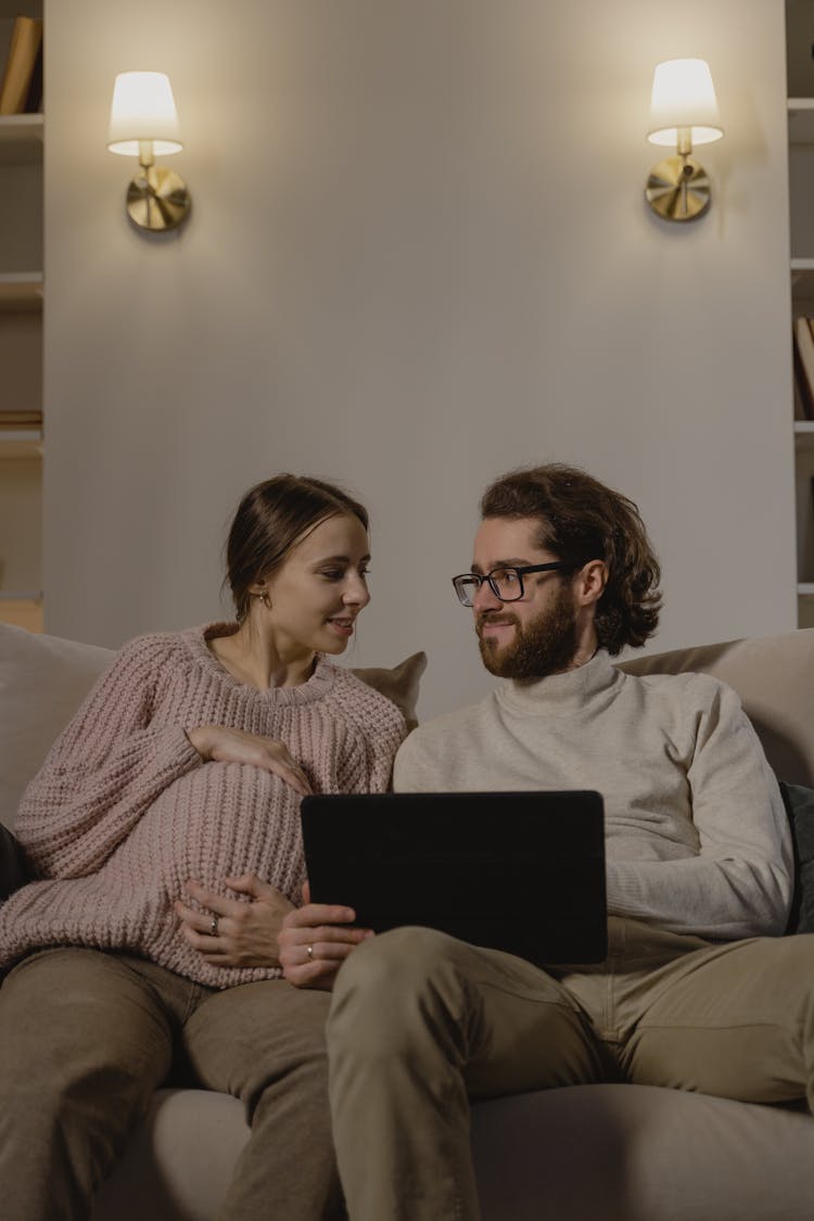 An Expecting Couple Sitting On Sofa Looking At Each Other