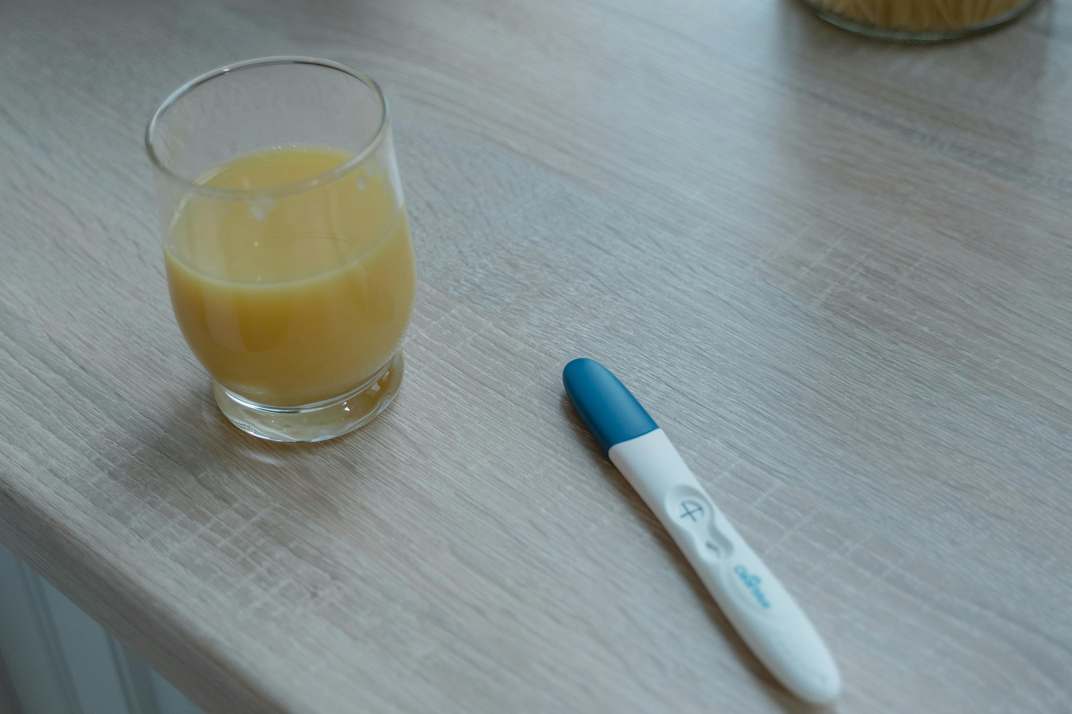 A Clear Drinking Glass Near the Pregnancy Test on a Wooden Table · Free