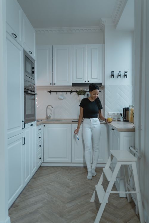 Free Adult woman stands in a stylish kitchen holding a glass of juice, conveying a sense of home and lifestyle. Stock Photo