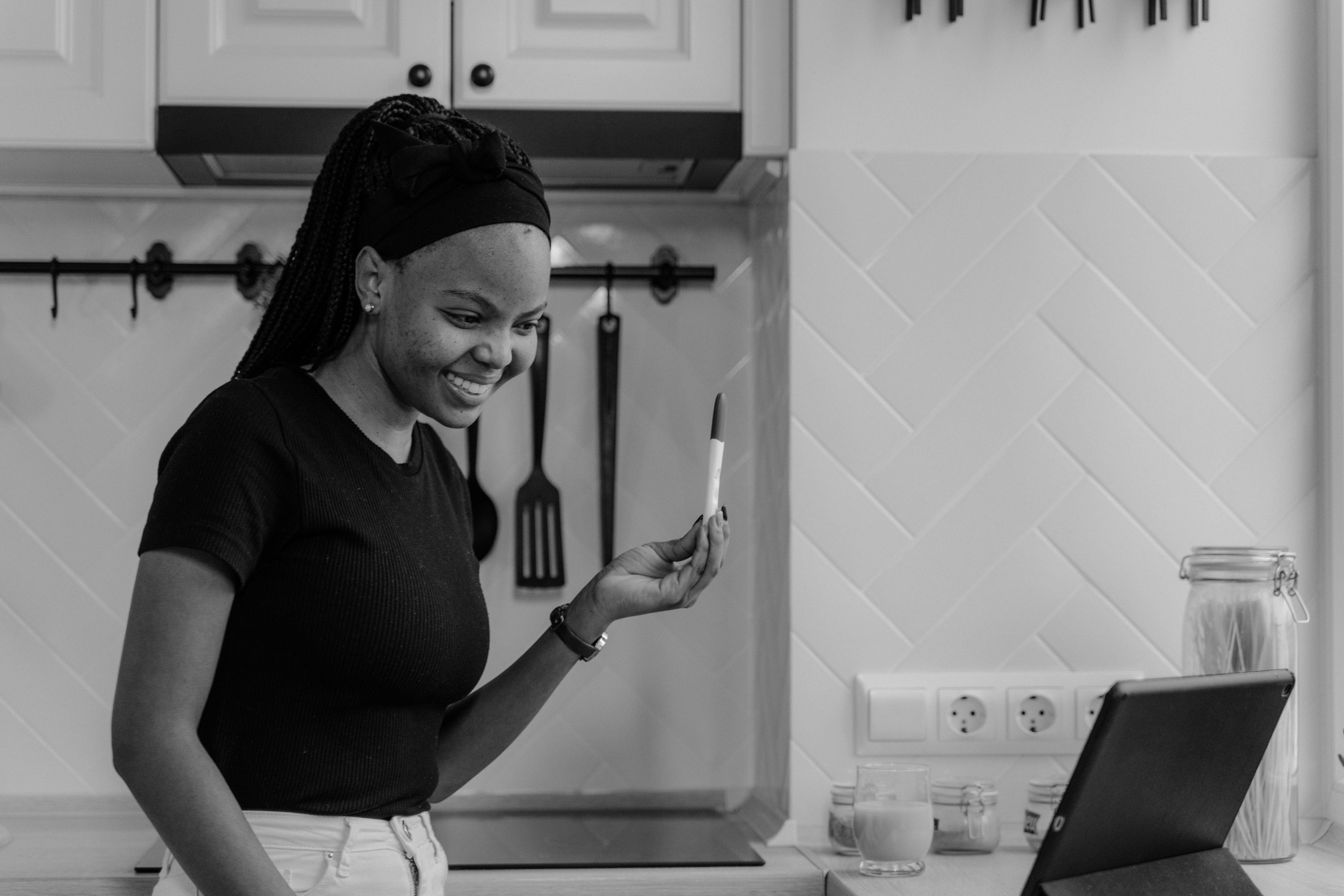 a grayscale photo of a woman in black shirt showing a pregnancy test while looking at the tablet