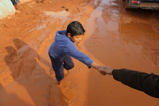 High angle of crop person holding hands with ethnic boy stuck in dirty puddle in poor village