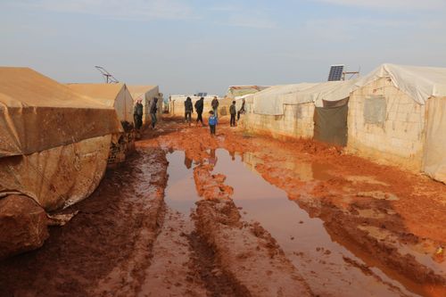 Free Group of distant adults and kids strolling on wet dirty ground with puddles near worn out tents in poor area Stock Photo