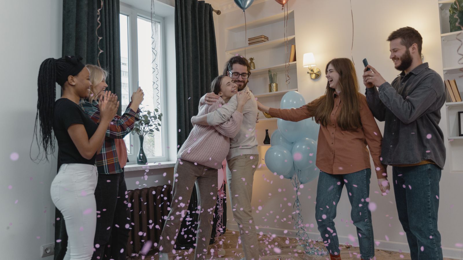 Vänner firar en babyshower med ballonger och konfetti hemma