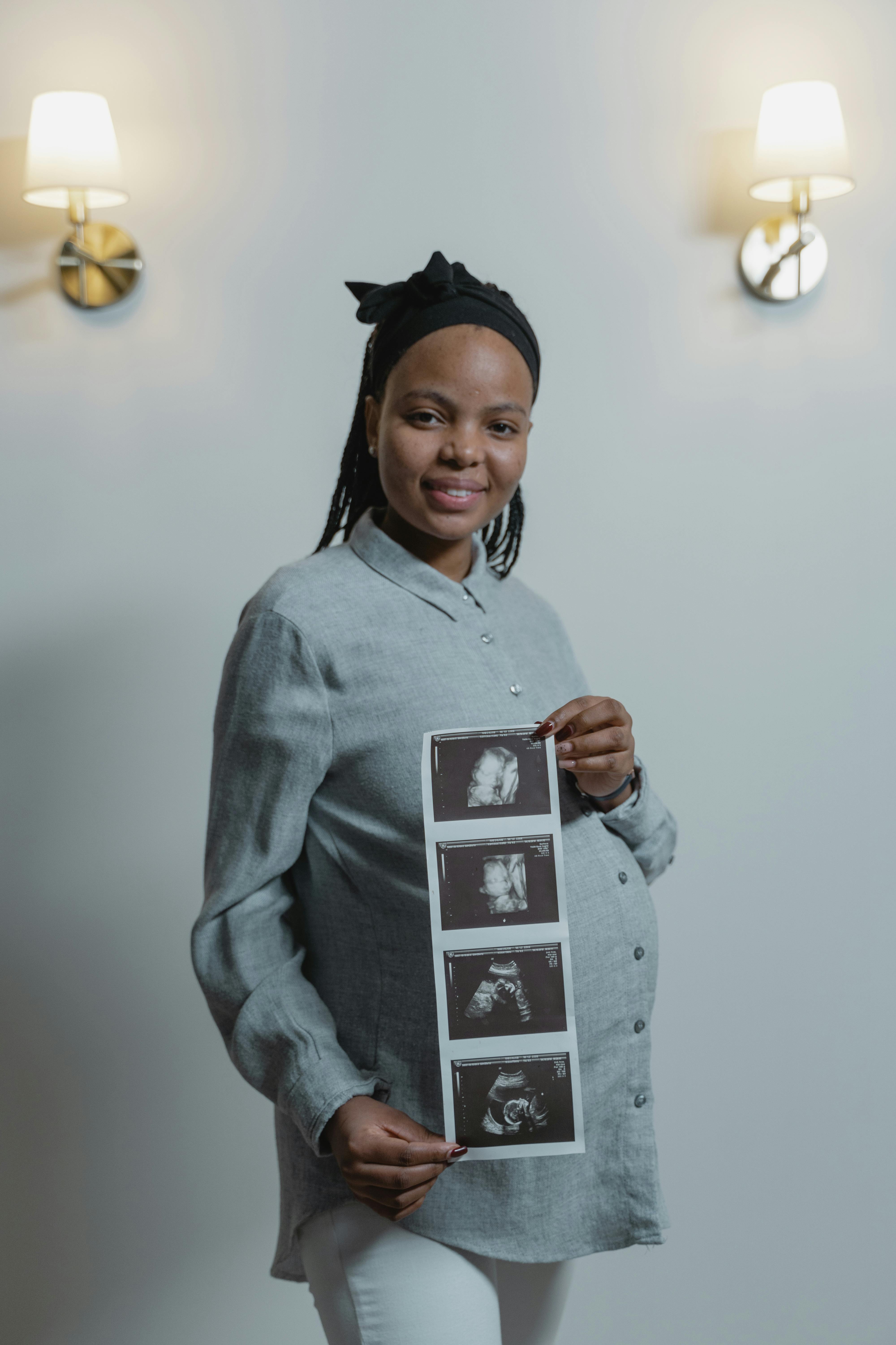  Smiling pregnant woman holding ultrasound images of her baby.
