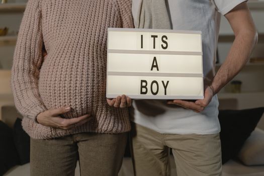 Pregnant couple indoors holding an 'It's a boy' sign, celebrating expecting a son.