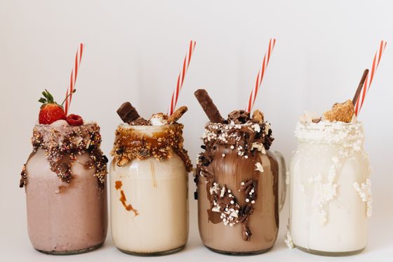 Four loaded milkshakes in jars with chocolate-coated rims, candy toppings and striped straws